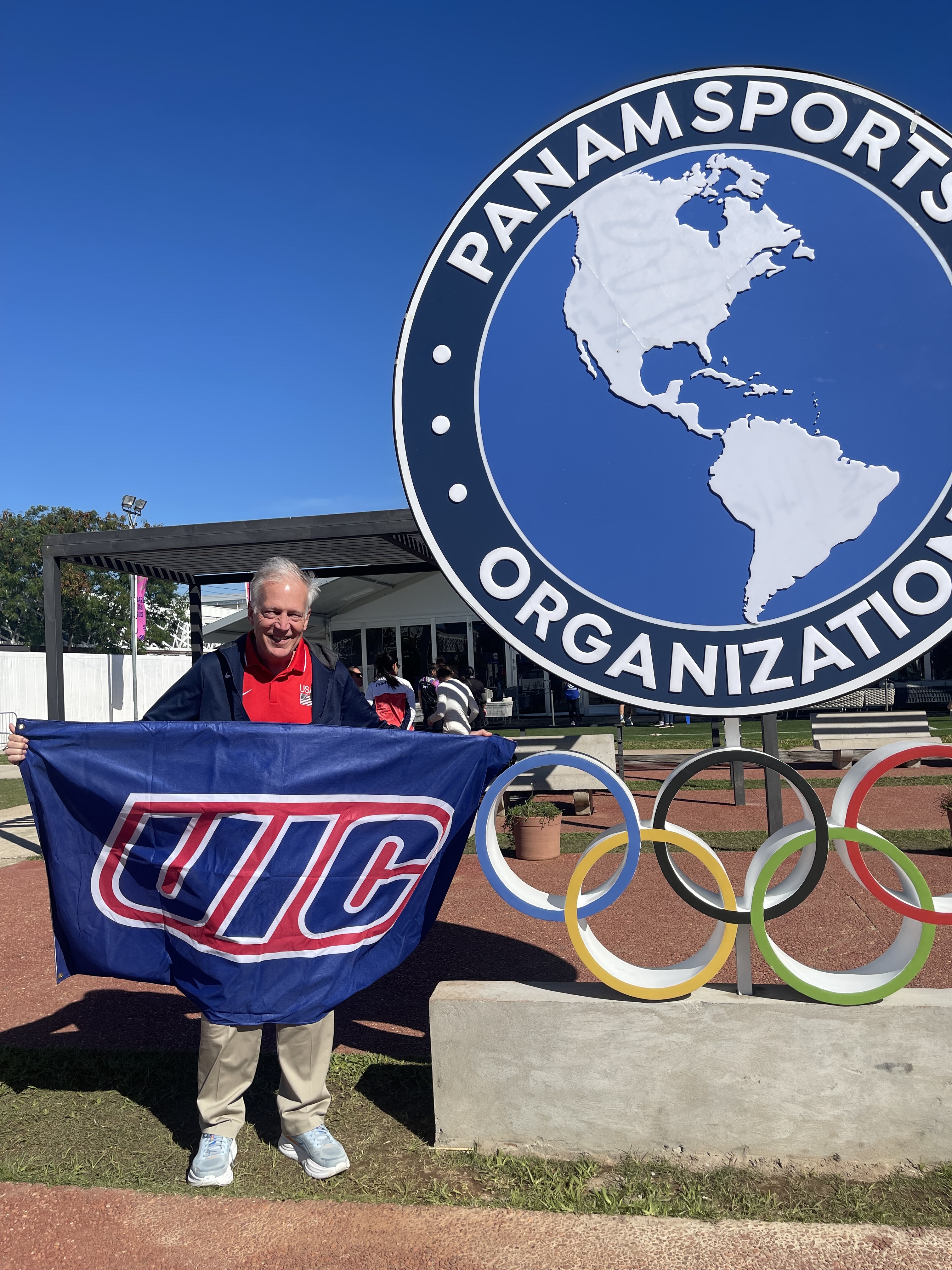A man holiding a UIC flag next to a PanAm Sports Organization sign