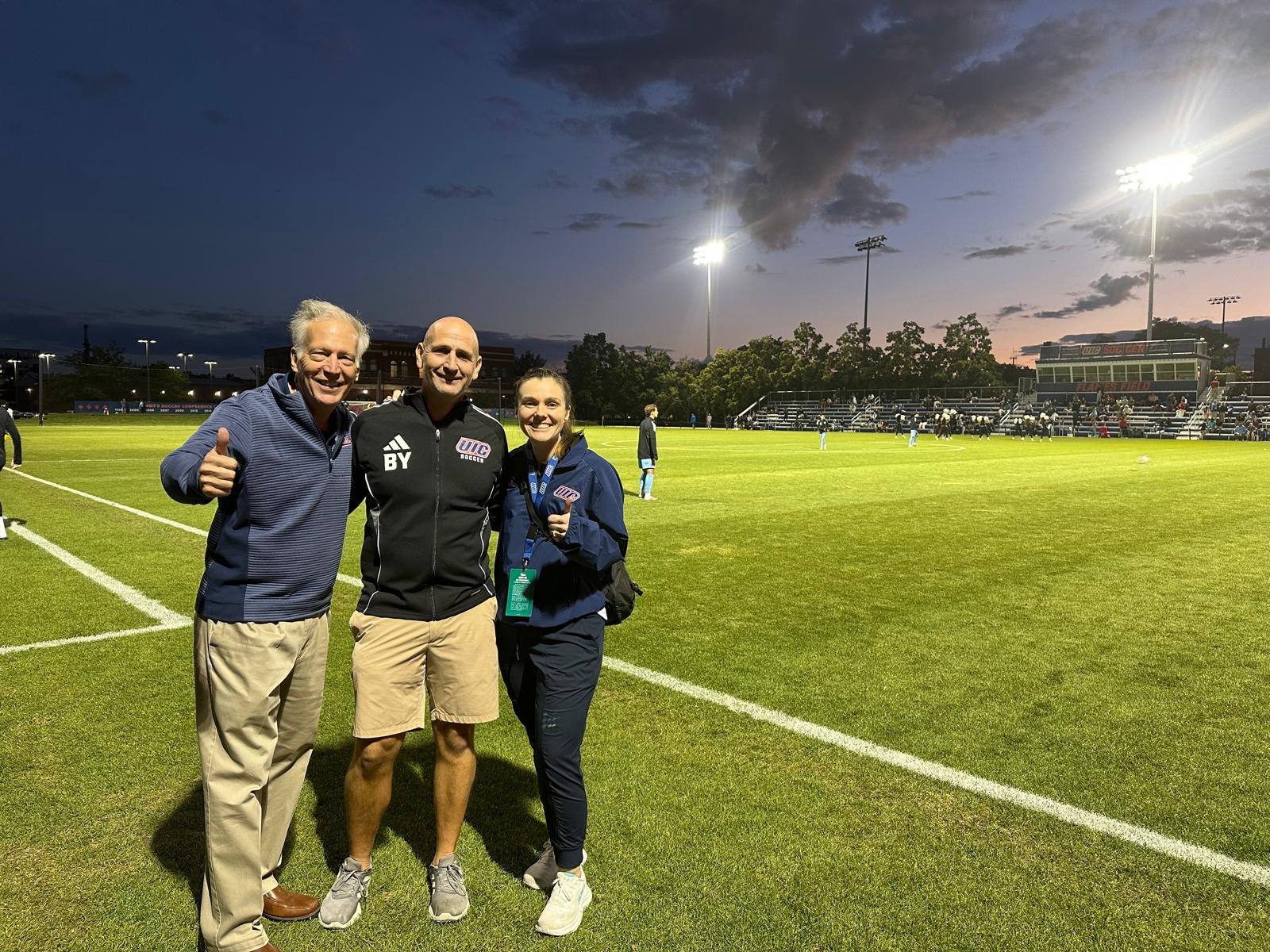 Two men and a woman stanging on a soccer field